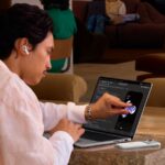 使用者坐在咖啡廳,用手指直接點 MacBook Pro 螢幕上的 app 畫面